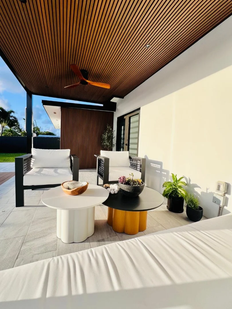 Covered patio seating area under a slatted timber ceiling, with a ceiling fan and low round tables